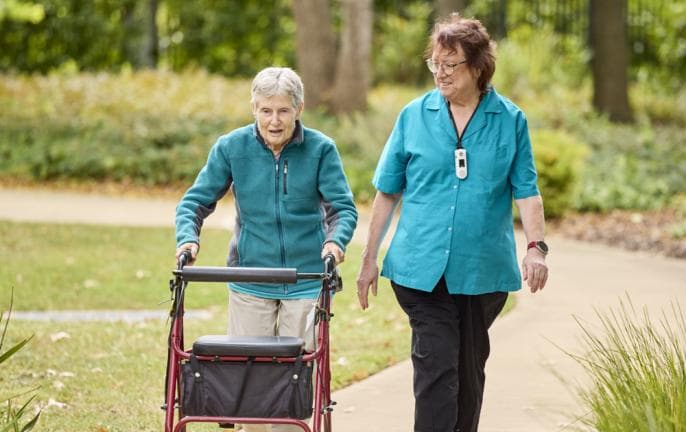 Older woman with walker and aged care worker walking outdoors