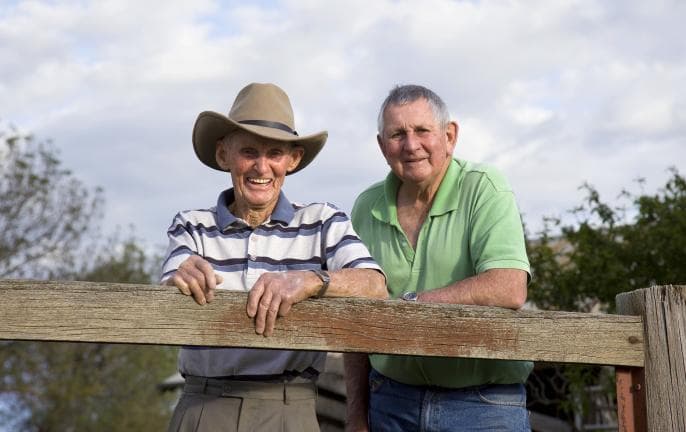 two smiling older men leaning on fence